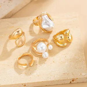 Detailed shot of Baroque pearl and gold water drop ring set arranged on stone surface.