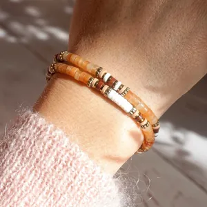 Close-up of stacked handmade beaded bracelets with natural orange semi-precious stones.