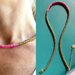Close-up detail of pink and gold beaded necklace with heart charm on teal background
