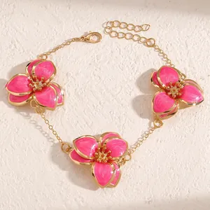 Detalle de una pulsera de cadena dorada con tres flores de esmalte rosa sobre fondo de piedra.