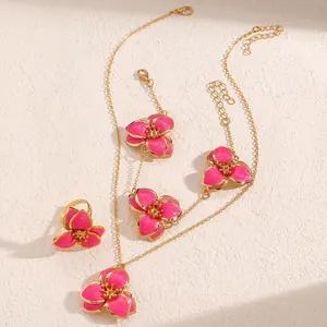 Detalle del conjunto de joyas doradas con colgantes de flores en esmalte rosa vibrante