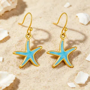 Primer plano de pendientes de estrella de mar dorados estilo océano sobre arena de mar