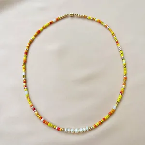 Bohemian rainbow seed bead necklace with irregular freshwater pearls on pink fabric.