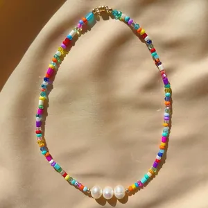 Close-up of bohemian colorful seed bead necklace with three pearls on silk fabric background.