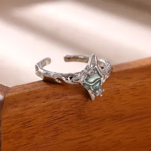 Close-up of a silver geometric open ring featuring green enamel and sparkling zircons