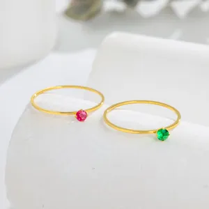 Detail view of two minimalist 14K gold ultra-thin rings with red and green gemstones