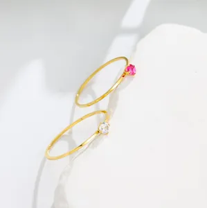 Close-up of two thin 14K gold minimalist rings with small red and clear gemstones