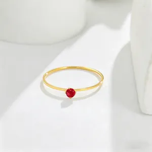 Close-up of a minimalist 14K gold ring featuring a delicate round red gemstone.