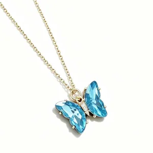 Elegante goldfarbene Halskette mit leuchtend blauem Schmetterlingsanhänger auf weißem Grund.