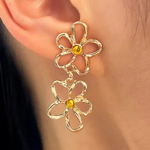 Detailansicht der goldenen Doppelblumen-Ohrringe mit Hohlraumdesign und gelben Mitten
