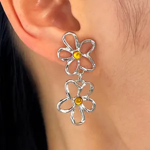 Detailansicht von silbernen hohlen Blumenohrringen mit gelben Steinen am menschlichen Ohr.
