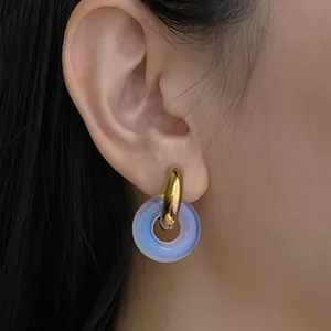 Primo piano di orecchini a cerchio d'oro con pendente a ciambella in vetro sfumato blu.