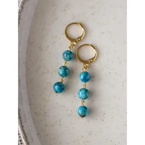 Dettaglio di orecchini a cerchio dorati con tre perle di pietra marmorizzata blu
