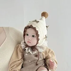 Primo piano di un bambino con un cappello di maglia crema con fiocco e pompon soffice.