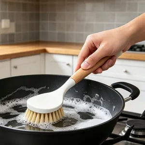 Kitchen wooden handle cleaning brush scrubbing a black frying pan with soapy bubbles