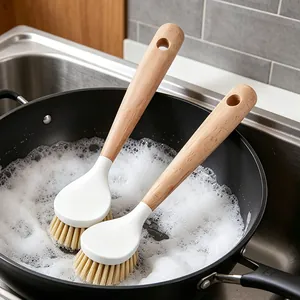 Macro view of a wooden handle dish brush cleaning a pot with thick soap foam.