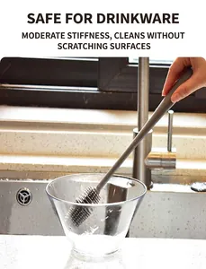 Close-up of long-handled silicone brush cleaning a clear glass cup in a kitchen sink
