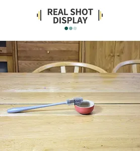 Detail shot of a blue long-handled silicone cup brush resting on a rustic wooden dining table