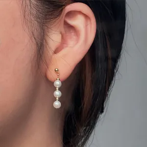 Primo piano di tre orecchini a goccia con perle d'acqua dolce naturali su un orecchio femminile