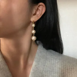 Dettaglio di tre orecchini pendenti con perle naturali d'acqua dolce indossati da una modella