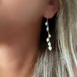 Dettaglio di eleganti orecchini a catena d'oro con perle naturali d'acqua dolce.