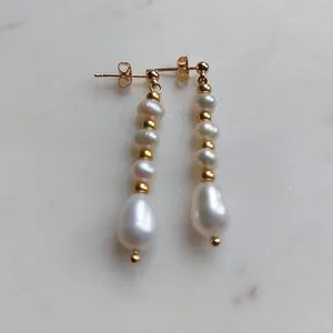 Dettaglio di eleganti orecchini pendenti con perle d'acqua dolce e perline placcate oro.