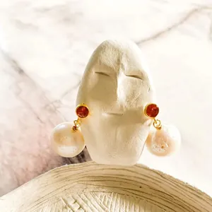Dettaglio degli orecchini in perle naturali con pietra rossa e finitura dorata.