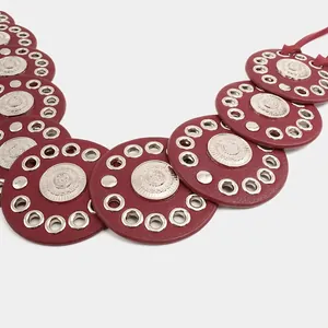 Close-up detail of a bohemian burgundy leather belt with silver grommets and medallions