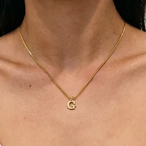 Detailed view of a gold titanium steel necklace featuring a letter G pendant on a neck.
