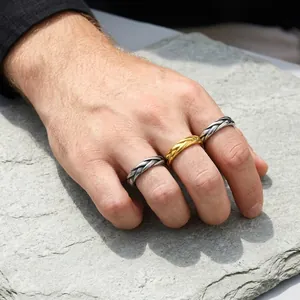 Close-up of three braided stainless steel rings in silver and gold on a male hand over stone