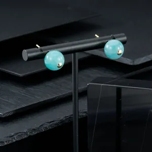 Macro detail view of round light blue semi-precious stone earrings with gold accents on stand