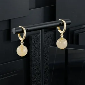 Detailed view of gold-plated hoop earrings with yellow gemstone drops on black stand