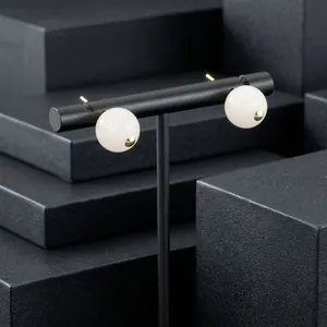 Detailed view of white semi-precious stone ball earrings on a black display stand