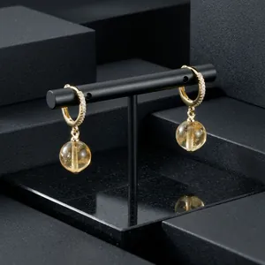 Close-up of gold-plated hoop earrings with amber gemstone pendants on a black stand