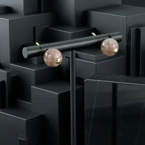 Close-up of spherical semi-precious stone earrings on a black minimalist geometric background