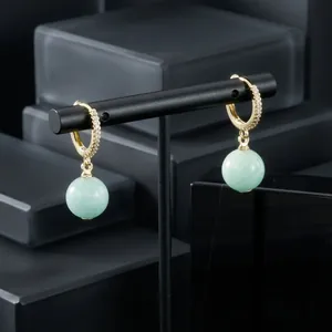 Detail view of gold-plated hoop earrings with CZ and green gemstone on stand