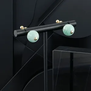 Close-up detail of light green semi-precious stone sphere earrings on a black jewelry stand