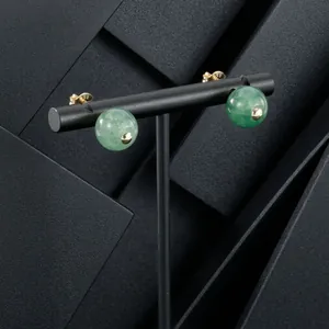 Macro view of green jade bead stud earrings with gold plating on black stand