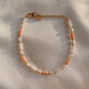 Primer plano de pulsera con perlas y piedras color melocotón sobre seda suave
