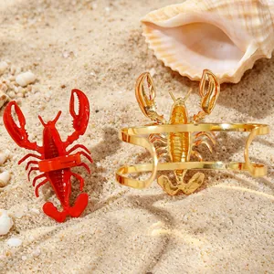 Detailed view of red and gold lobster jewelry pieces on a sunny sandy beach with shells.