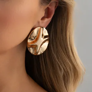 Close-up of gold irregular textured stud earring on model, showing metallic wave details.
