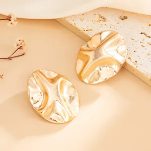 Close-up of gold geometric pleated earrings with irregular wavy surface texture.