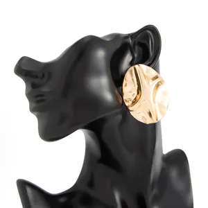 Detailed view of large golden geometric ripple stud earrings on a black mannequin