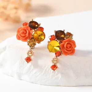 Close-up detail of floral stud earrings with orange resin roses and faceted warm-toned crystals