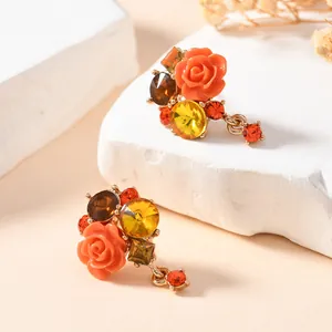 Macro detail of floral stud earrings featuring an orange resin rose and vibrant crystals