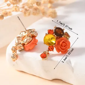 Detailed view of floral stud earrings with orange rose and yellow crystals