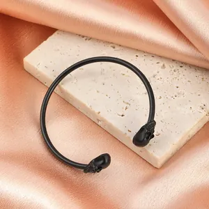 Détail d'un bracelet jonc gothique noir mat avec deux têtes de mort aux extrémités.