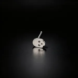 Detailed macro shot of a silver-tone skull-shaped nose stud piercing on a black surface.