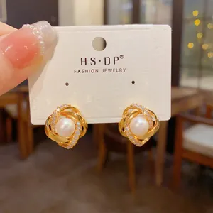 Dettaglio di eleganti orecchini a perno intrecciati in oro con perla e pietre in micro-pave