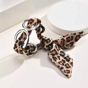Detail view of leopard print silk scarf intertwined with silver geometric metal rings